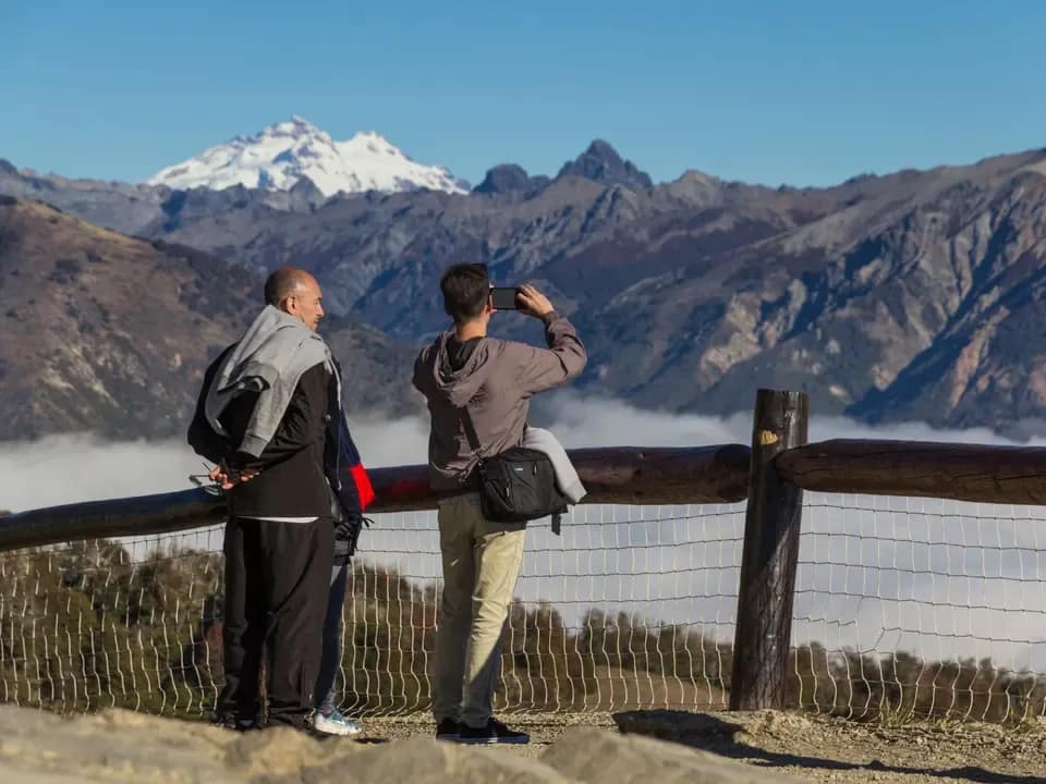 Dos personas de espaldas admirando las montañas desde un balcón del Teleférico Cerro Otto