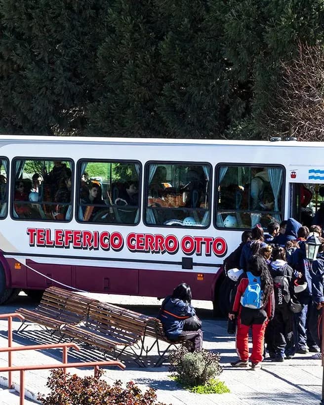 Bus turístico gratuito con logo del Teleférico Cerro Otto en el estacionamiento de la base con gente descendiendo.